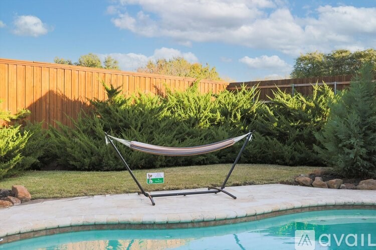 A hammock is suspended between two poles in a backyard with a pool.