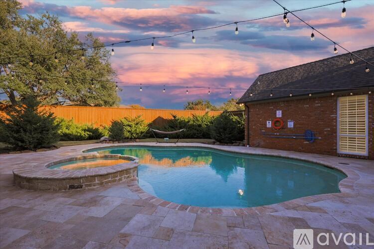 A pool surrounded by a stone patio and a wooden fence.