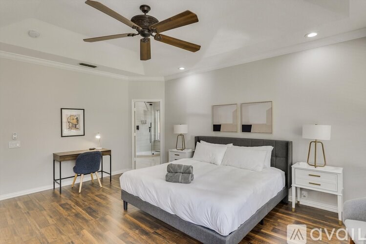 A bedroom with a bed, a chair, a table, and a ceiling fan.