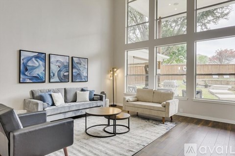 A living room with a grey couch, a black chair, a round table, and a painting on the wall.