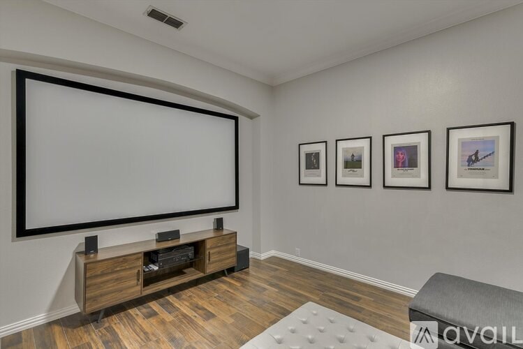 A living room with a large screen, a wooden entertainment center, and three framed pictures on the wall.
