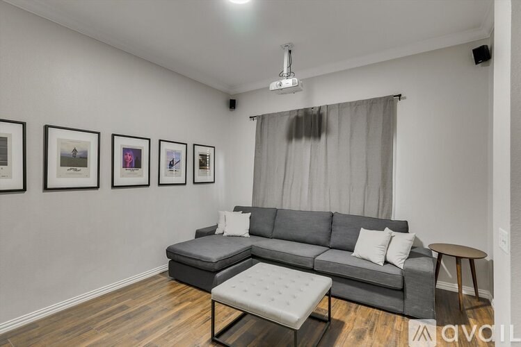 A living room with a grey couch, a small ottoman, and pictures on the wall.