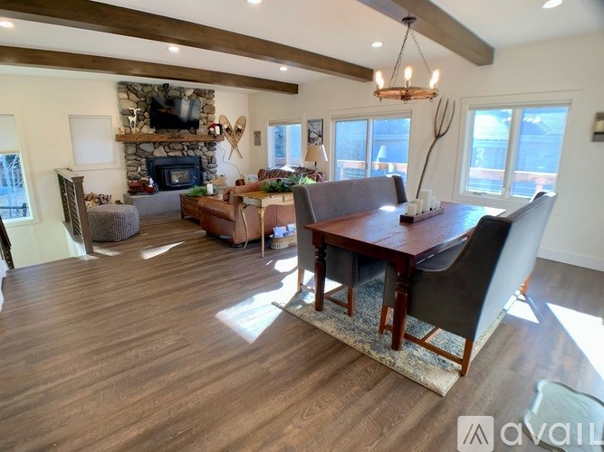 A large, well-lit living room with a wooden floor and a stone fireplace.