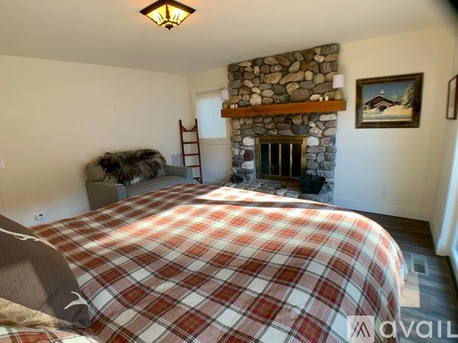 A bedroom with a plaid bedspread and a stone fireplace.