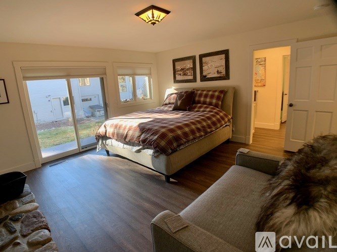 A bedroom with a bed, a couch, and a window overlooking a yard.