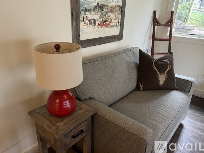 A red lamp sits on a wooden table next to a grey couch.