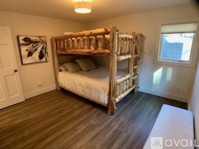 A wooden bunk bed with a white mattress and pillow is in a room with wooden flooring and a white door.