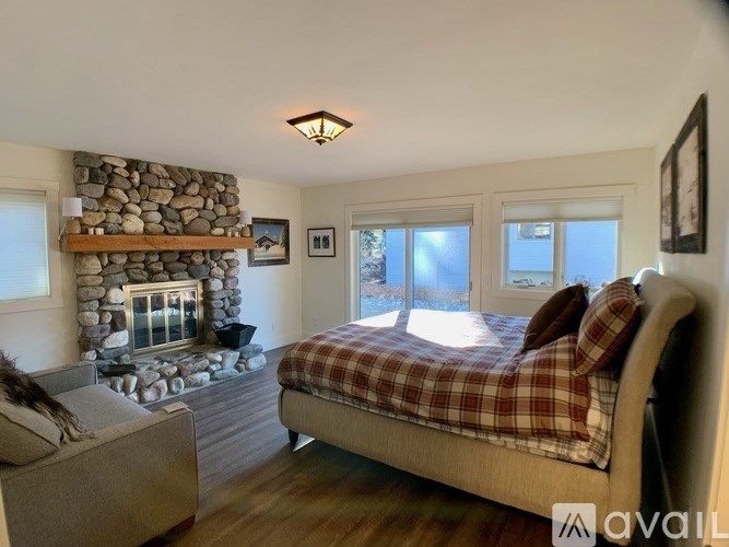 A bedroom with a stone fireplace and a bed with a plaid comforter.