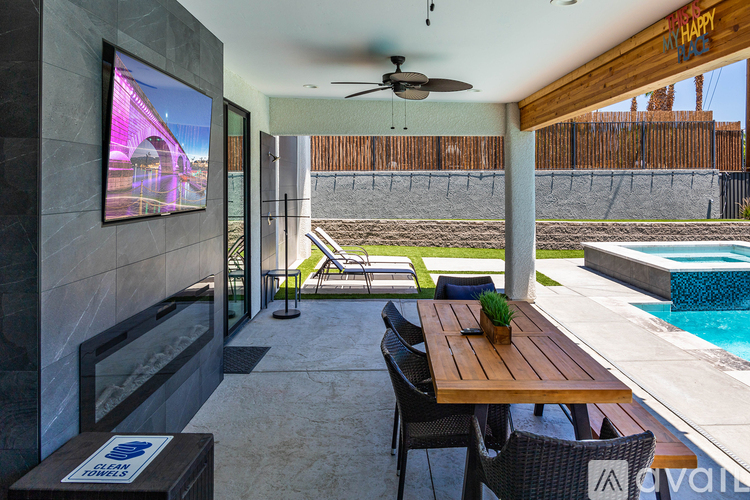 A modern outdoor dining area with a wooden table and chairs, a television, and a pool.