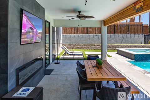 A modern outdoor dining area with a wooden table and chairs, a television, and a pool.