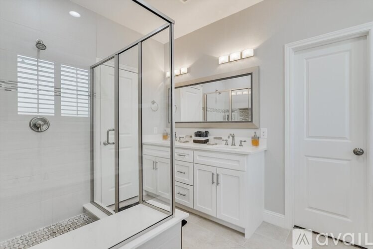 A bathroom with a walk-in shower, white cabinets, and a large mirror.
