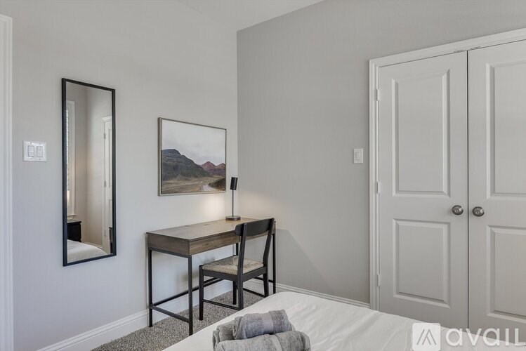 A bedroom with a bed, desk, chair, and a painting on the wall.
