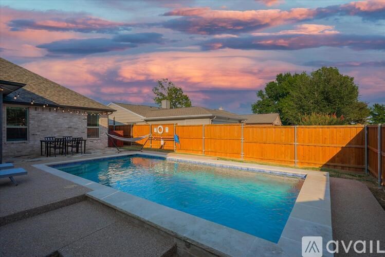 A pool surrounded by a concrete patio and a wooden fence.