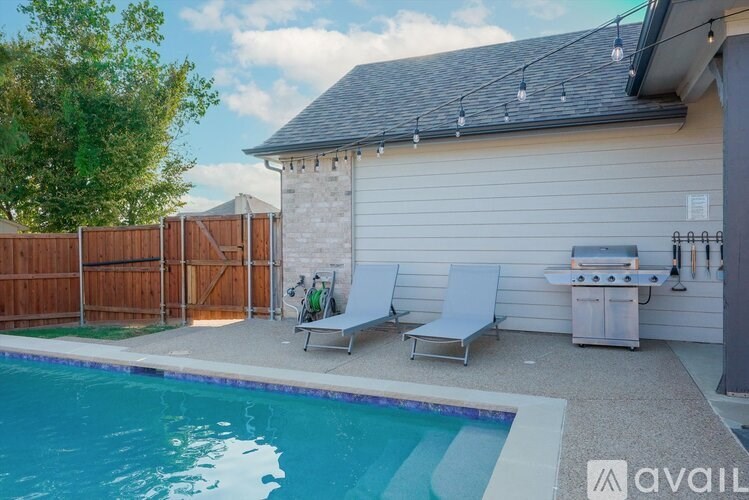 A pool with a sun lounger and a grill outside a house.
