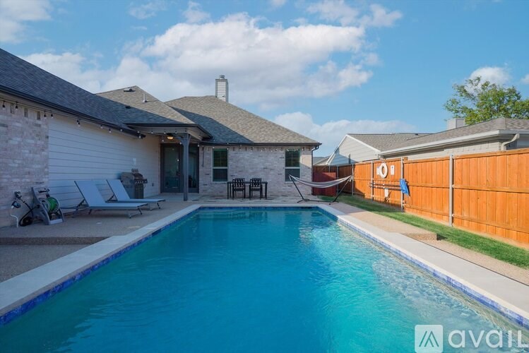 A pool in a backyard with a house and lawn chairs.