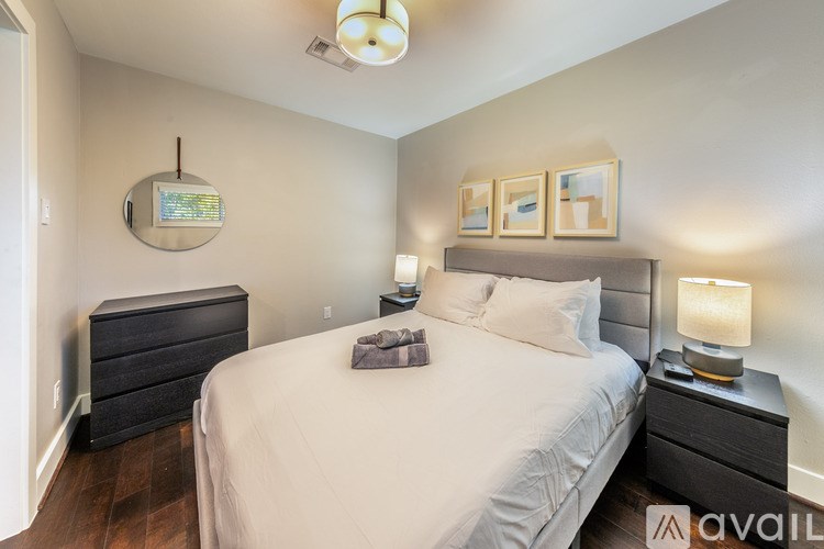 A bedroom with a large bed, a nightstand with a lamp, and a dresser with a mirror.