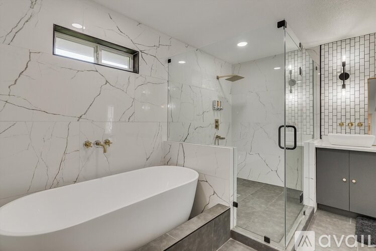 A white bathtub sits in a marble-walled bathroom with a walk-in shower.