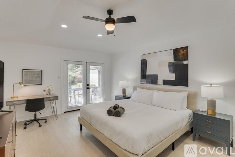 A bedroom with a large bed, a desk with a chair, and a ceiling fan.