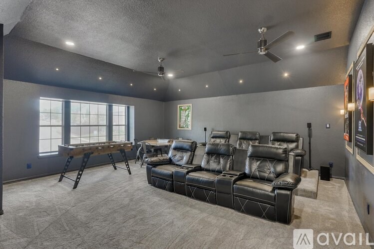 A spacious home theater with a row of black leather seats and a wooden table.