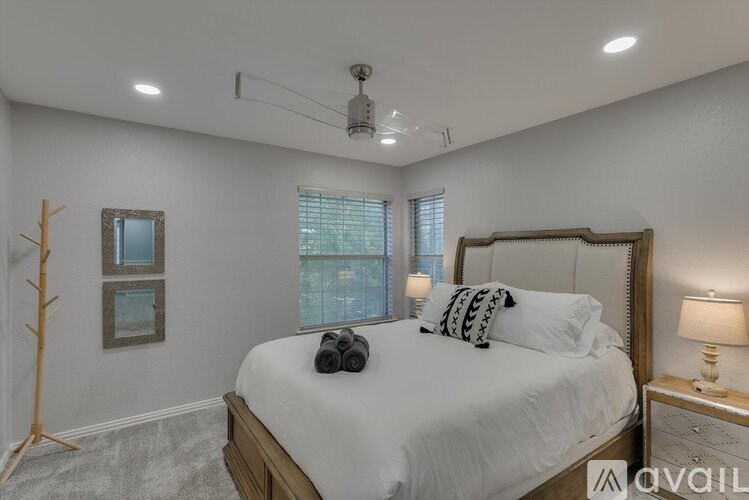 A bedroom with a large bed, a window with blinds, and a nightstand with a lamp.