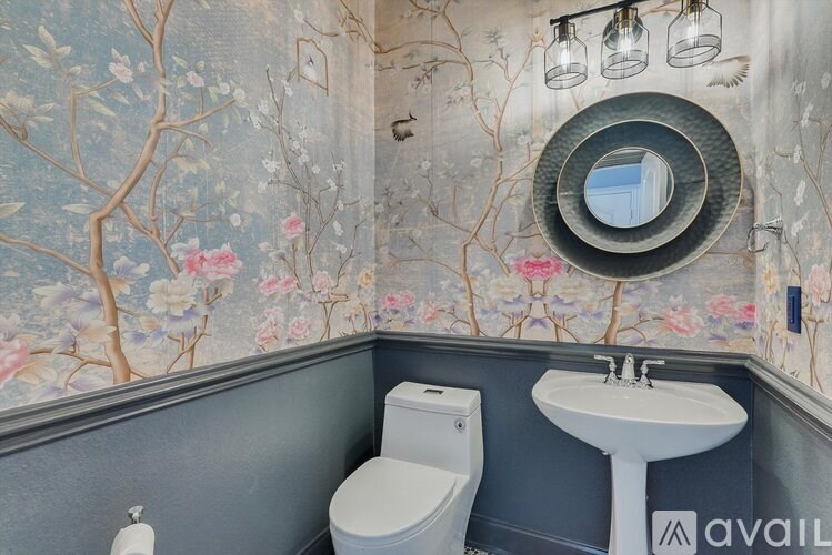 A bathroom with a floral wallpaper and a round mirror above a sink.