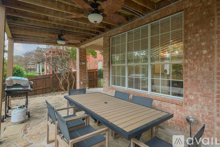 A wooden table and chairs are set up on a patio with a brick wall and a ceiling fan.