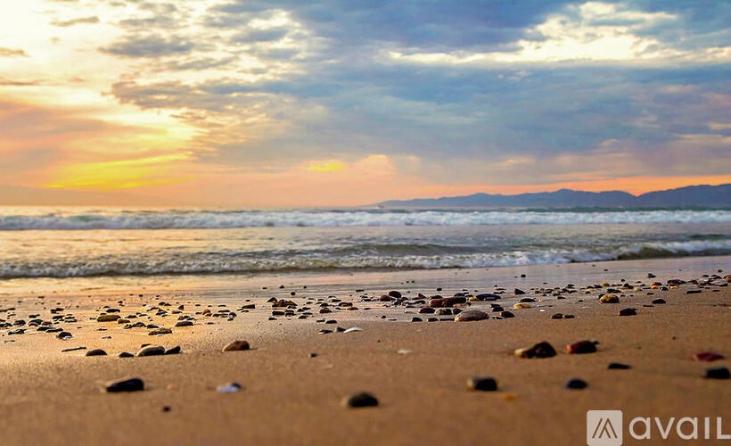 A beach at sunset with scattered rocks on the sand.