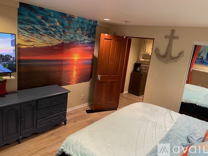 A bedroom with a large bed and a painting of a sunset on the wall.