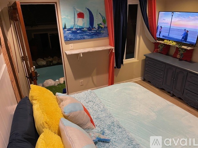 A bedroom with a bed, a TV, and a painting of a sailboat on the wall.