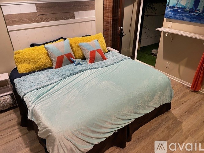 A bed with a blue comforter and four pillows with different patterns.