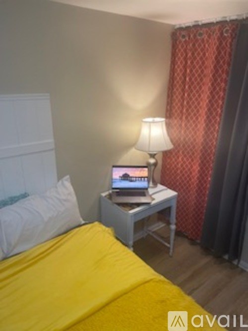 A bedroom with a bed, a nightstand with a lamp and a book on it.