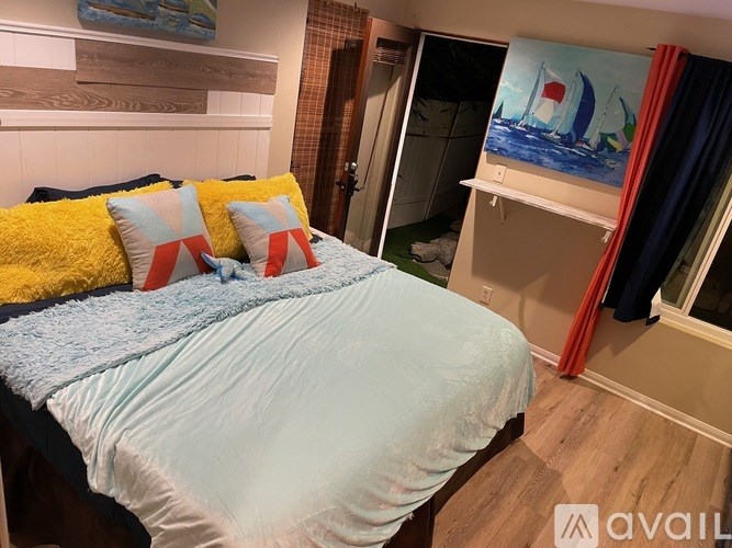 A bed with a blue comforter and yellow and red pillows.