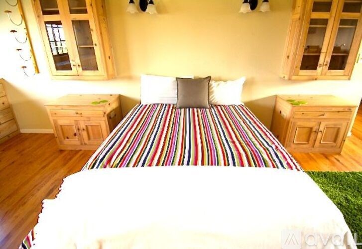 A bed with a striped bedspread is in the center of a room with wooden floors and furniture.