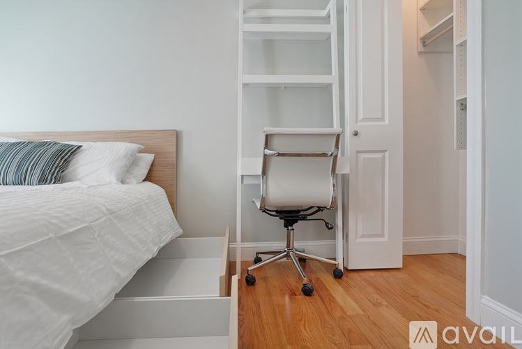 A white bedroom with a bed, chair, and shelves.
