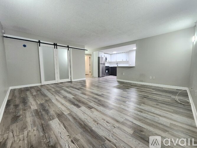 A spacious room with wood flooring and sliding glass doors leading to a kitchen.