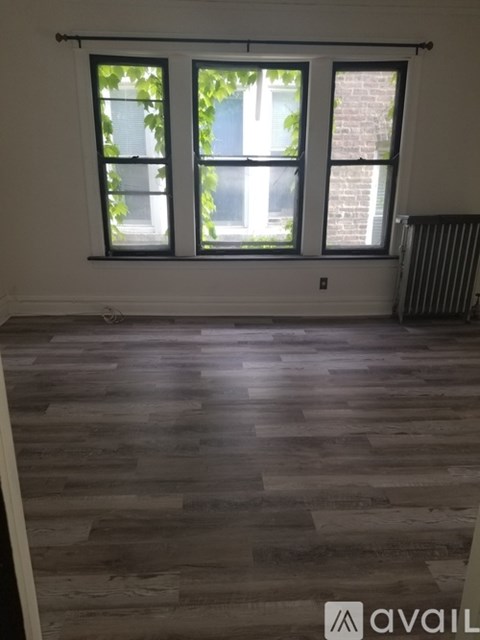 A room with wooden flooring and a window showing a view of a building and trees.