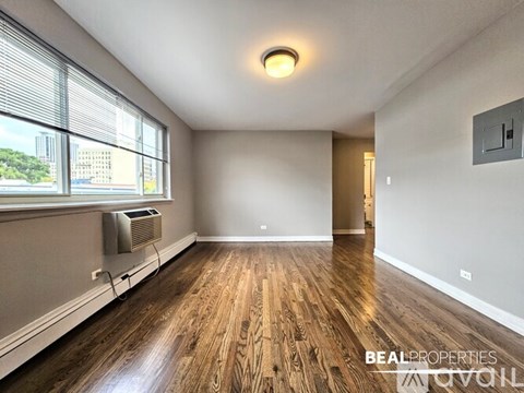 A spacious room with wooden flooring and a window with blinds.