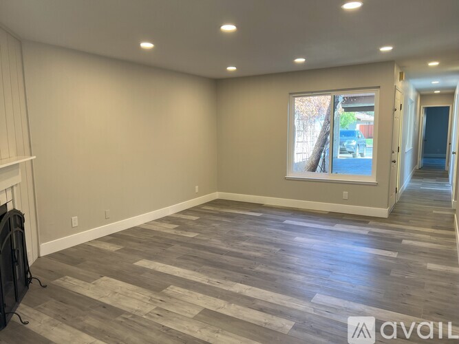 A spacious room with wooden flooring and a fireplace on the left side.