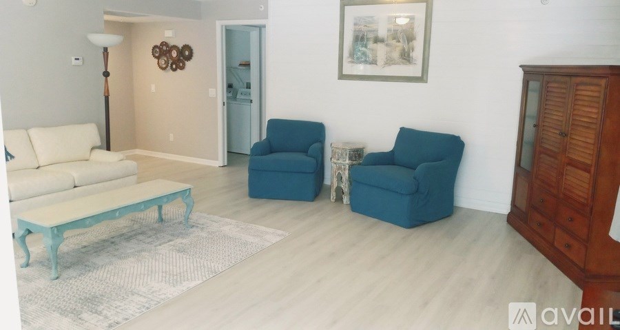 A living room with a white couch, blue chairs, and a wooden cabinet.