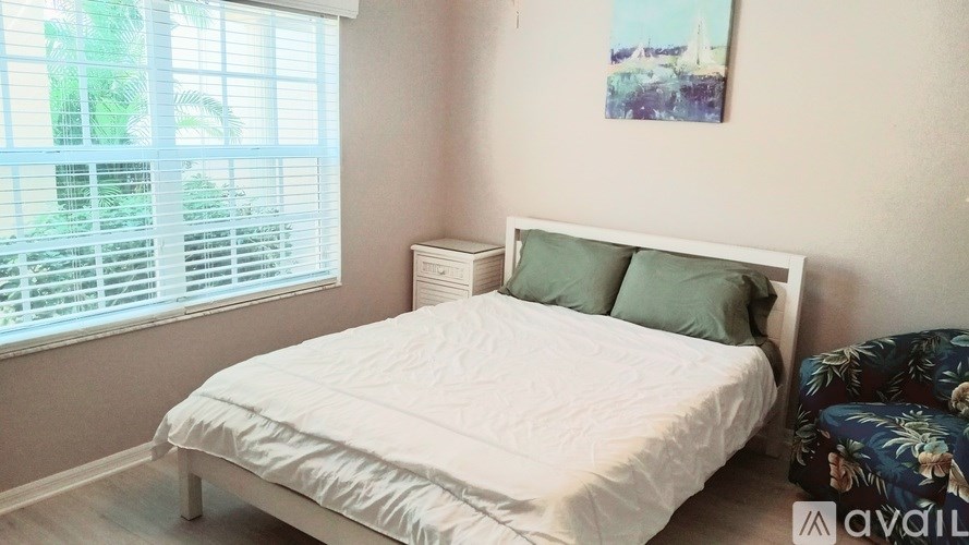 A white bed with a white headboard and two green pillows in a room with a window.