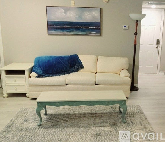 A living room with a white couch and a painting on the wall.