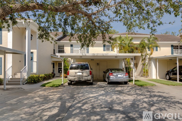 A white two-story house with a carport and a tree in front.