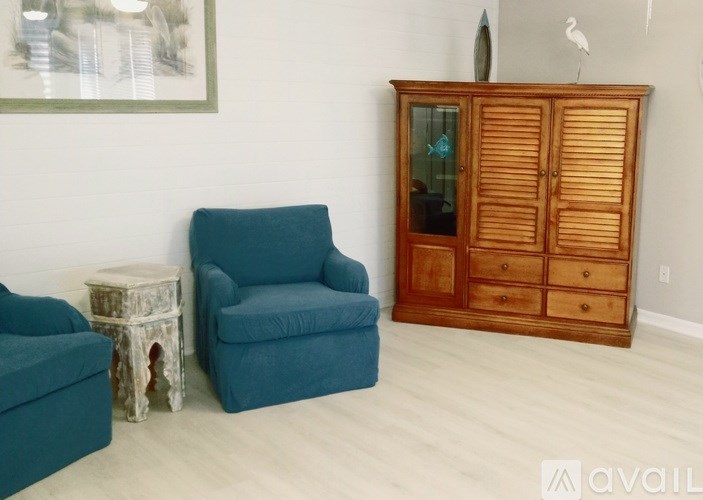 A room with a blue chair, a wooden cabinet, and a white stool.