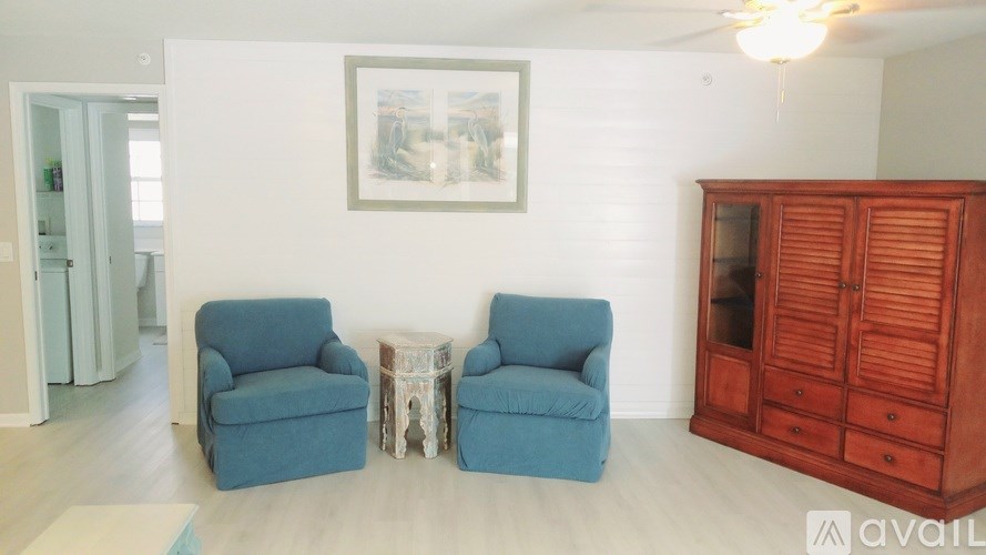 Two blue chairs are placed in a room with a wooden cabinet and a framed picture on the wall.