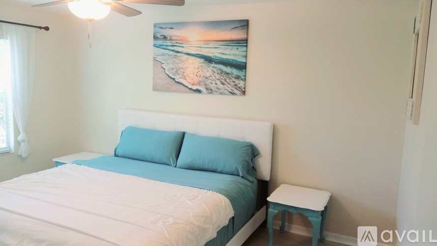 A bedroom with a bed, a ceiling fan, and a picture of a beach on the wall.