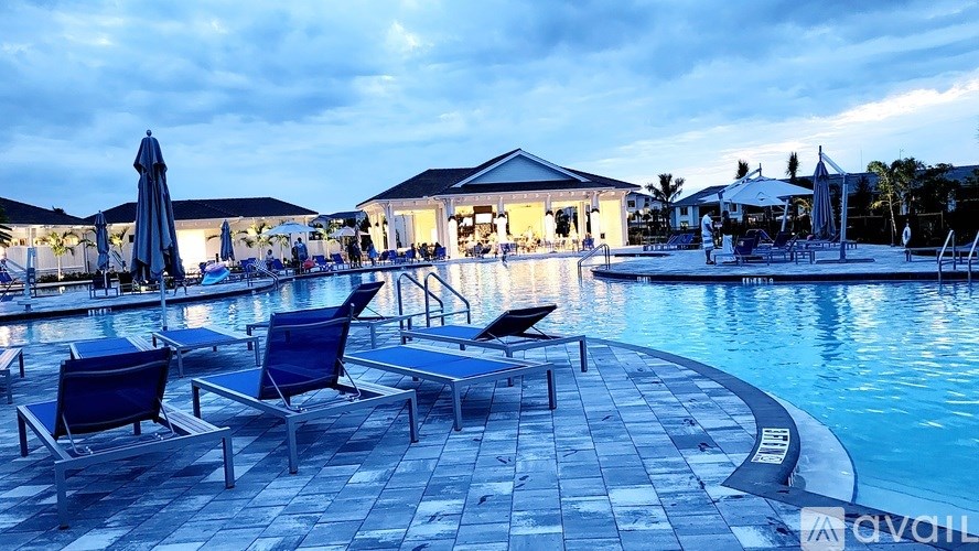 A poolside area with lounge chairs and umbrellas is lit up at dusk.