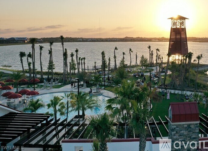 A sunset view of a pool area with palm trees and a tower.
