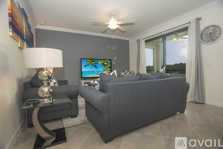 A living room with a grey couch, a glass table with a lamp, and a painting on the wall.