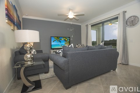 A living room with a grey couch, a glass table with a lamp, and a painting on the wall.