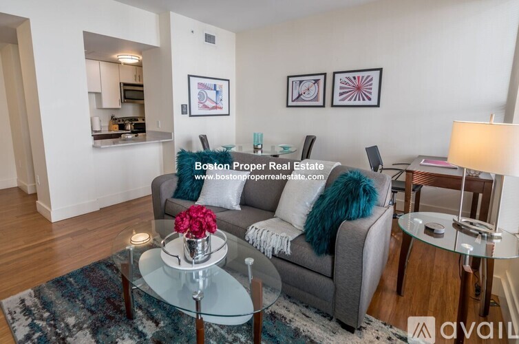 A living room with a grey couch and a glass table with a vase of flowers on it.